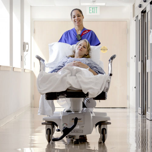 Infirmière poussant un lit occupé d'une patiente dans un couloir d’hôpital